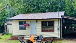 Ein kleines, eingeschossiges Haus mit Metalldach, einer Veranda mit Feuerstelle und einem überdachten Bereich auf der rechten Seite.
