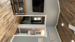 Ein modernes Loft-Zimmer mit großem Fernseher, Holzboden, eingebautem Sitzplatz und kleinem Fenster.