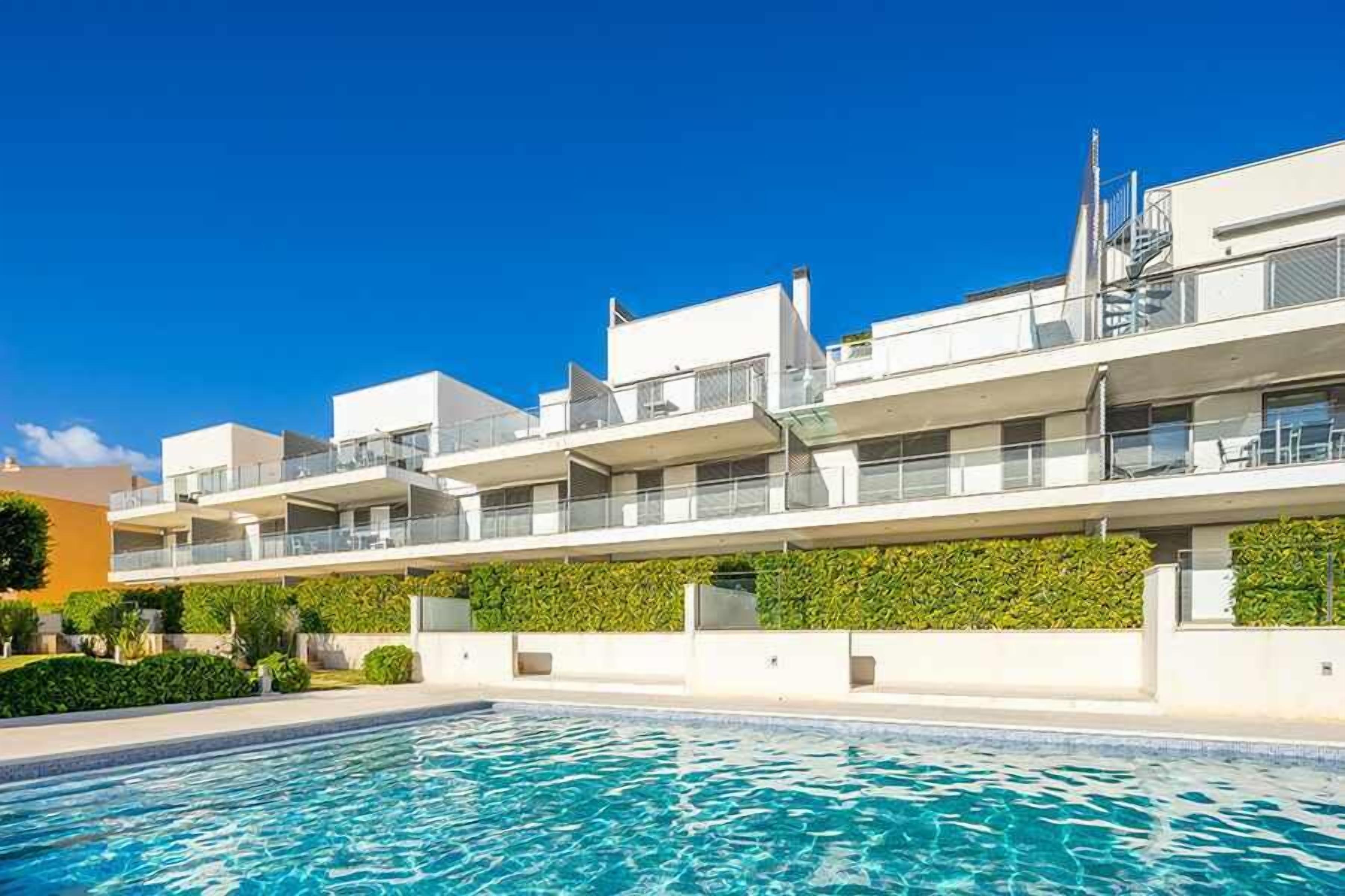A modern hotel with a pool, multiple balconies, and a clear blue sky.