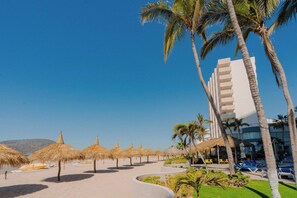 A beach resort with thatched umbrellas, palm trees, and a modern building with balconies. - Sunset Palace Beach Hotel (Mazatlán)