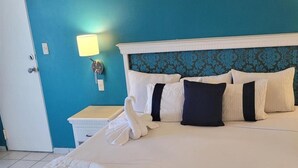 A hotel room with a teal wall, a white bed with multiple pillows, a bedside lamp, and a white swan-shaped towel. - Sunset Palace Beach Hotel (Mazatlán)