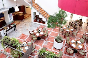 Enjoy meals in the dining area with round tables and chairs, surrounded by a potted plant and a staircase.
