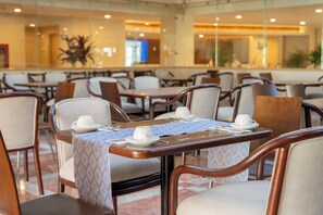 A hotel dining area with tables set for service, chairs, and a large window in the background. - Sunset Palace Beach Hotel (Mazatlán)