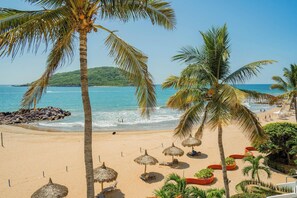 Ein Strand mit Palmen, Reetdachschirmen und Liegestühlen.