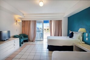 A hotel room with a bed, a desk, a TV, and a view of the outside. - Sunset Palace Beach Hotel (Mazatlán)
