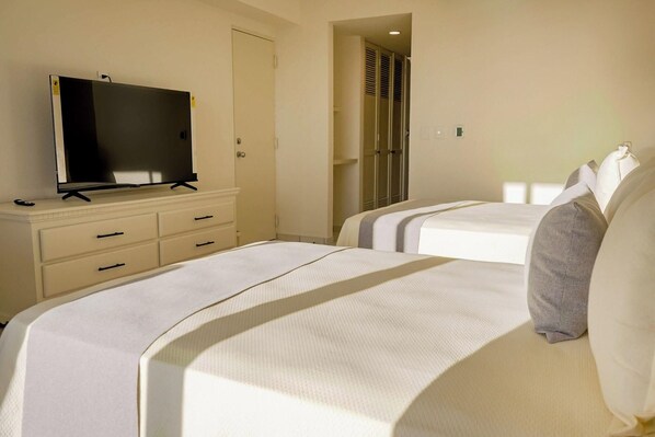 A hotel room with two beds, a TV on a dresser, and a walk-in closet. - Sunset Palace Beach Hotel (Mazatlán)
