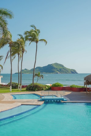 Relax by the oceanfront pool surrounded by lush greenery and palm trees.