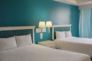 A hotel room with two beds, white linens, a nightstand, two wall-mounted lamps, and a teal-colored wall. - Sunset Palace Beach Hotel (Mazatlán)