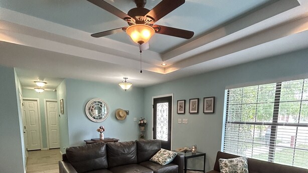 A spacious living room with a ceiling fan, a dark brown leather sofa, a grey armchair, and a wooden coffee table. - whole 3 bedroom home (Eagle Pass)