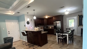 A modern kitchen with a central island, dining area with chairs, and a large window. - whole 3 bedroom home (Eagle Pass)
