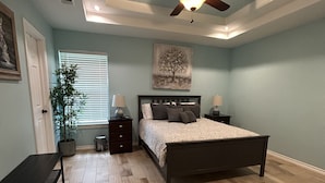 A bedroom with a bed, bedside tables, a ceiling fan, a window with blinds, a potted plant, and a painting on the wall. - whole 3 bedroom home (Eagle Pass)