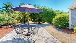 A patio with a round table and chairs, an umbrella, and a small building in the background. - Charming Chatham Cottage  (Chatham)