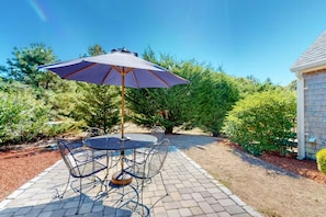 Relax in the serene patio area with a round table, four chairs, and a central umbrella, surrounded by lush greenery.