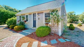 A single-story house with a front porch, a small garden with trimmed bushes, and a clear sky. - Charming Chatham Cottage  (Chatham)