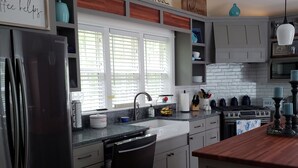 Une cuisine moderne équipée d’un réfrigérateur en acier inoxydable, d’un lave-vaisselle et d’une cuisinière. On y trouve des armoires en bois et une fenêtre avec des stores.