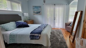 Une chambre à coucher comprenant un lit, une table de chevet, une commode, une chaise, un miroir et une fenêtre avec des stores.