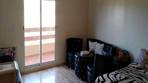 A room with a sliding glass door leading to a balcony, a black leather sofa, a small round table, and a zebra-patterned bedspread.