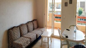 A living room with a patterned sofa, a small table, and a balcony with a view.