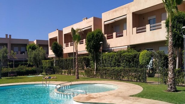 A swimming pool with a curved edge, surrounded by a well-maintained lawn and palm trees.