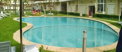 A swimming pool surrounded by a well-maintained lawn, with lounge chairs and umbrellas.