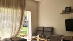 Een moderne woonkamer met een bank, twee fauteuils, een flatscreen televisie en een schuifpui naar een balkon.