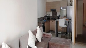 Un espacio habitable compacto con kitchenette, un sofá con cojines y una zona de comedor con una silla.