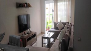 Una sala de estar con televisión de pantalla plana, un sofá, una mesa de centro y un comedor con mesa y sillas.
