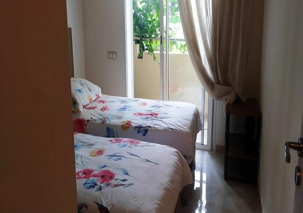 Une chambre avec deux lits, une porte-fenêtre coulissante donnant sur l’extérieur et une petite table.