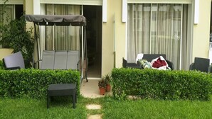 Un espacio al aire libre techado con una mecedora, una mesita pequeña y plantas en macetas.
