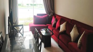 Un salon avec un canapé rouge, une table basse en verre et une vue sur une piscine et la verdure environnante.