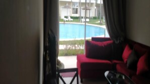 Une pièce avec un canapé rouge, une table basse en verre et une vue sur une piscine et un espace de détente extérieur.