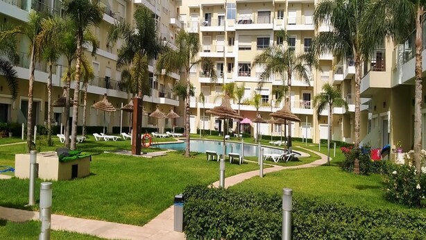 Un hôtel à plusieurs étages doté d’une piscine entourée de palmiers et de chaises longues.