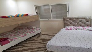 Una camera da letto con un letto a castello, un letto singolo, una finestra con persiane e un tappeto decorato.