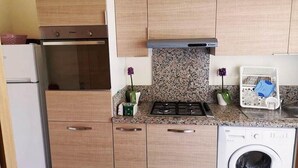 Una cucina compatta con mobili in legno, forno ventilato, piano cottura a gas, microonde e lavatrice.