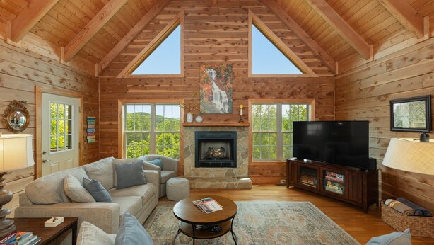 L’intérieur d’une cabane en rondins, avec une cheminée, un téléviseur et un coin salon confortable.