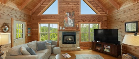 A log cabin interior with a fireplace, television, and cozy seating area.