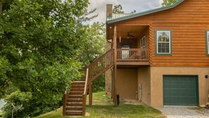 A two-story log cabin with a balcony, a stone chimney, and a green garage door. - Sunrise Ridge Lodge in Hendersonville NC (Hendersonville)