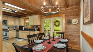 Un intérieur en bois avec une table à manger pour quatre personnes, des appareils de cuisine et un lustre.