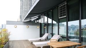 Una terraza en la azotea con sillones de descanso, una mesa de madera y vistas a la ciudad.