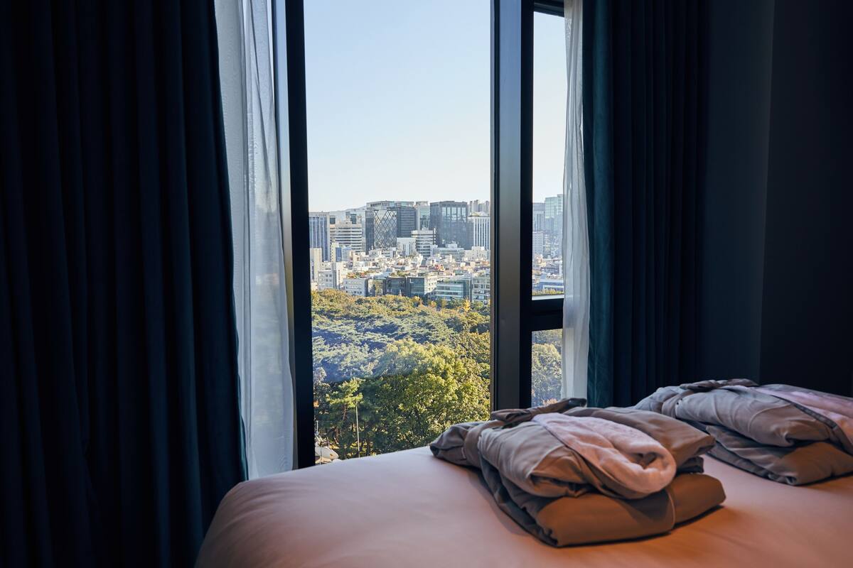 A hotel room with a large window offering a city view.