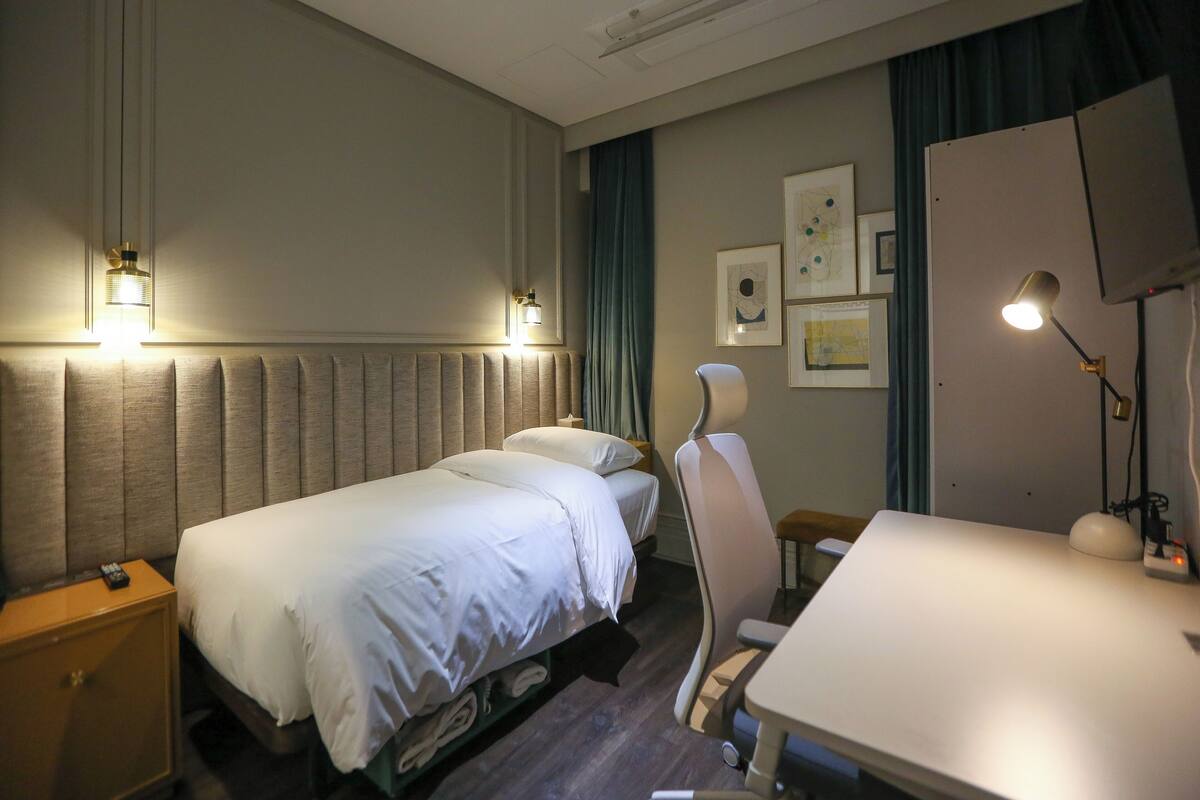 A hotel room with two beds, a desk, a chair, a wardrobe, and artwork on the wall.