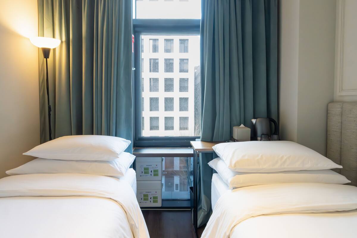 A hotel room with two beds, a desk, a lamp, and a window with curtains.