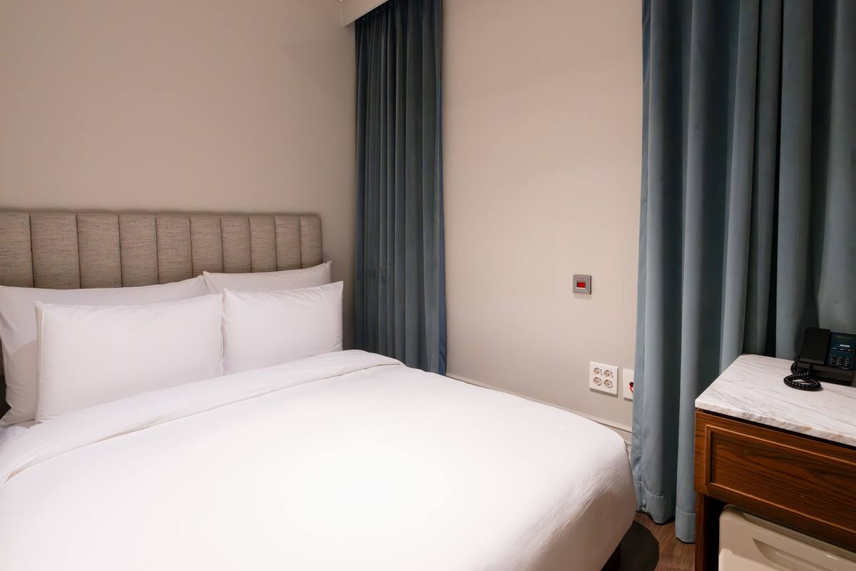 A hotel room with a bed, a nightstand, a telephone, and a wall socket.