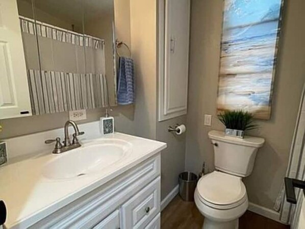 A bathroom with a white sink, a mirror, a toilet, and a framed artwork on the wall.