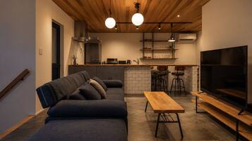 Un espace de vie moderne comprenant un canapé, une table en bois, un téléviseur et un coin cuisine avec un bar.