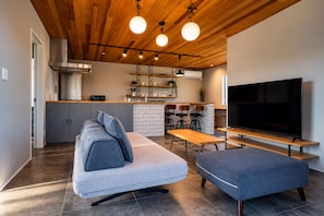 A modern living space with a sofa, ottoman, dining table, and a TV. - TOTONOI Villa YAE (Motobu)