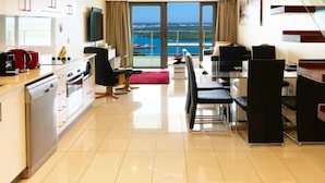 A modern kitchen with a dining area, large windows with a view of the sea, and a flat-screen TV.