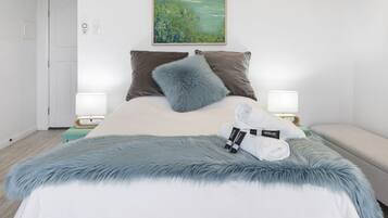 A modern bedroom with a large bed, a ceiling fan, a painting, and a nightstand with a lamp.