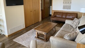 Een woonkamer met een houten salontafel, een bank en een aan de muur bevestigde televisie.