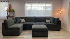 A modern living room with a sectional sofa, a small ottoman, a floor lamp, and a plant on a side table. - Entire Newly Renovated House in North Pomona (Pomona)